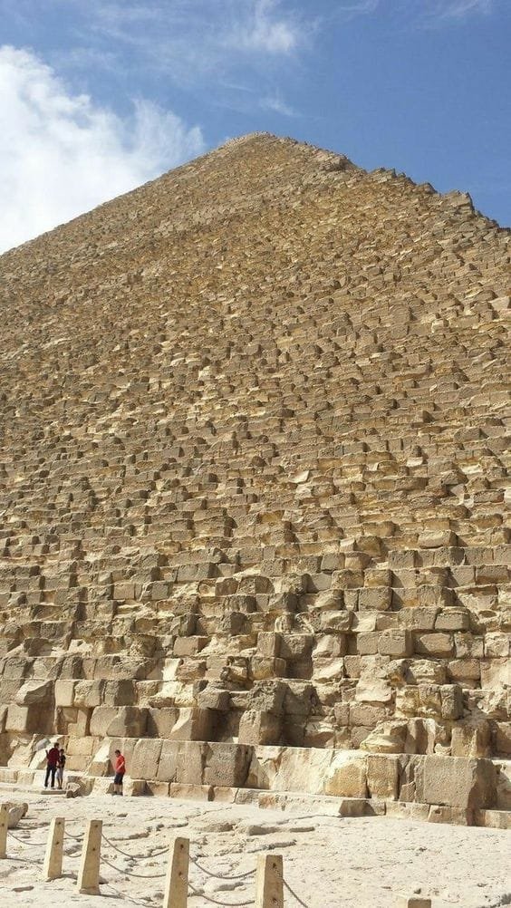 a large pyramid with many blocks with Great Pyramid of Giza in the background