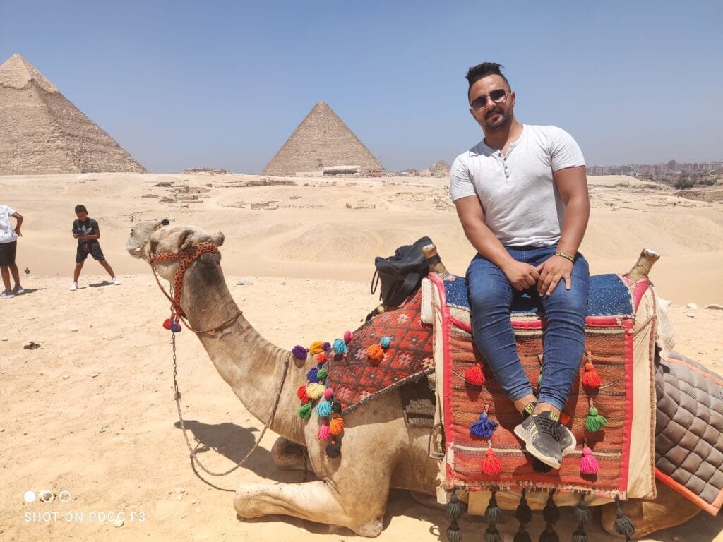 Manager on a camel with the Pyramids of Giza in the background, with Egypt Tour Magic.